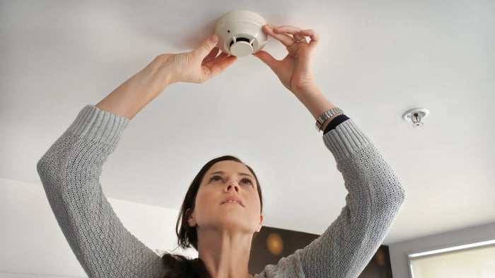 mujer colocando un detector de humos en el techo