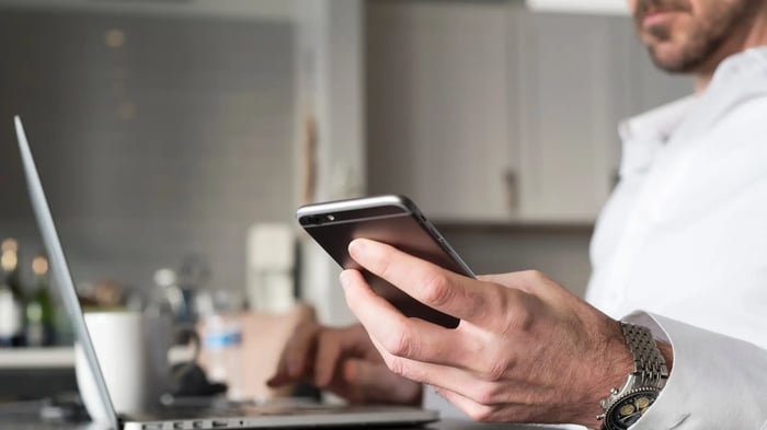 Persona utilizando un teléfono móvil junto a un ordenador portátil en un entorno de trabajo doméstico