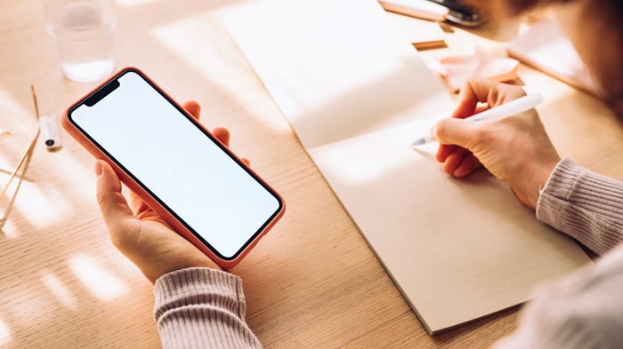 persona con un móvil en una mano y un bolígrafo en la otra escribiendo