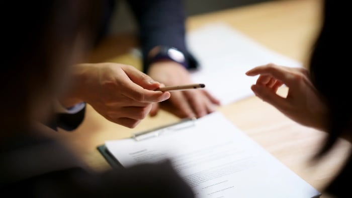 Primer plano de dos personas intercambiando un bolígrafo sobre un documento con texto, colocado en una mesa de trabajo