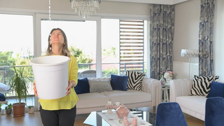 Persona en un salón sosteniendo un cubo mientras cae agua del techo.