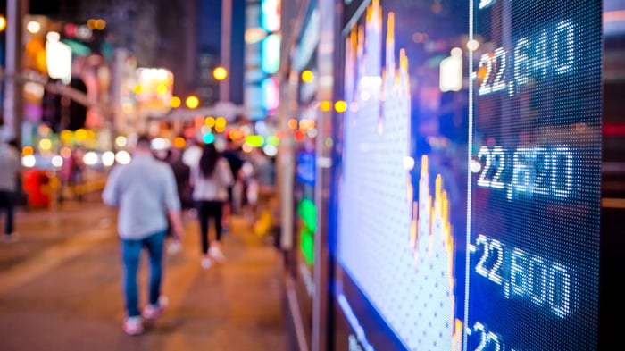 personas difuminadas andando por la calle con una pantalla reflejando gráficos de inversión