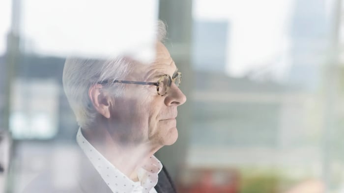 Persona adulta mayor con gafas vista de perfil a través de un cristal, en un entorno interior luminoso