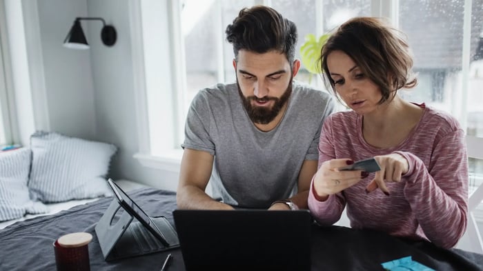 pareja de hombre y mujer sentados delante de un ordenador con una tarjeta de crédito