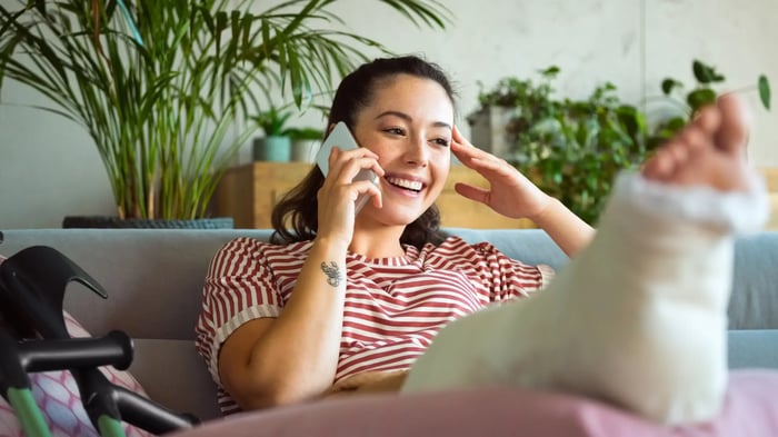 Mujer sonriendo hablando con el móvil con una pierna escayolada