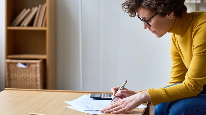 mujer escribiendo en una mesa baja con una calculadora y papeles