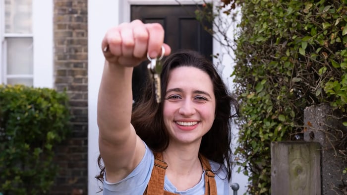 chica sonriendo mostrando las llaves de una casa en la mano