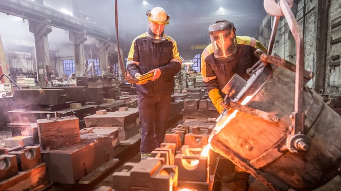Trabajadores industriales con equipos de protección vertiendo metal fundido en una fábrica metalúrgica