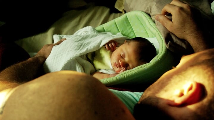 Bebé durmiendo en una cuna junto a una persona adulta.