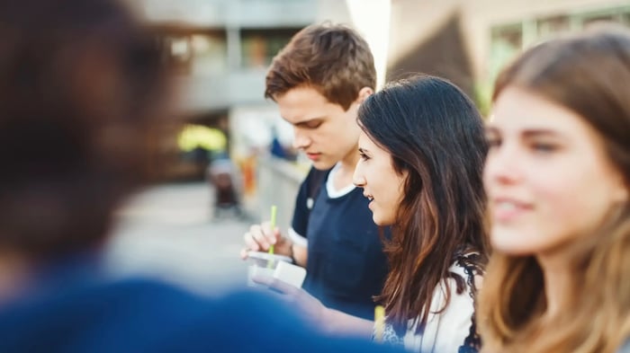 tres adolescentes en la calle, uno de ellos bebiendo de un vaso